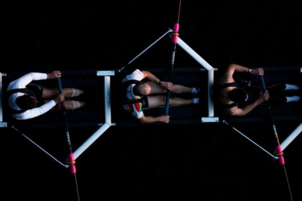 Collaborate: A crew team of four people rowing against a dark background