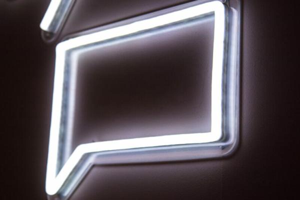 An image of a glowing white neon light shaped like a voice balloon against a black background