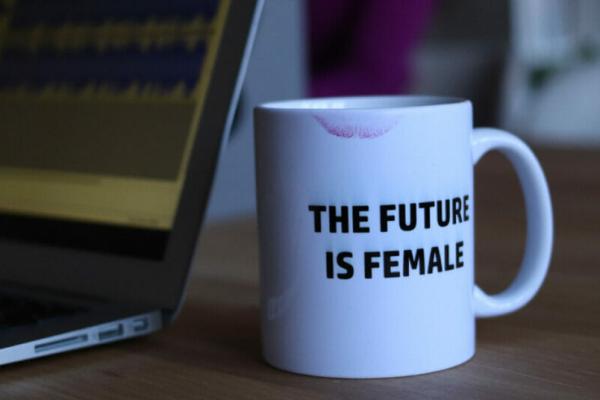 A desk with a laptop and a white mug with a lipstick stain that says The Future is Female