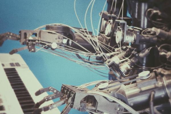 A robot made of silver metal playing a piano keyboard in front of a blue background