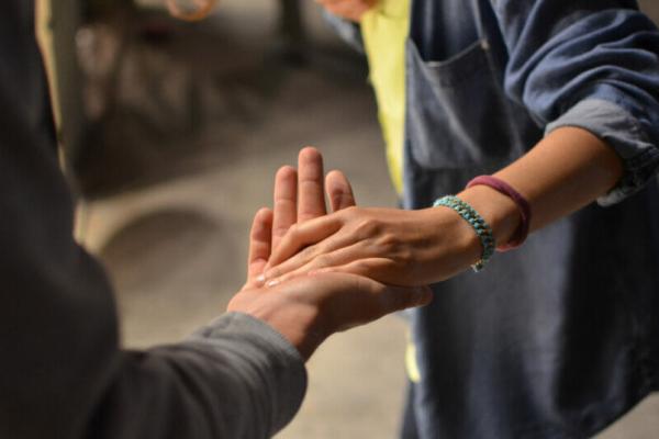 A man lending a woman a helping hand, leading her with their palms together. She is wearing a blue denim shirt and he has a dark gray suit jacket. You cannot see their faces - just their hands and midsections.