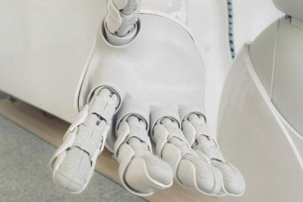 An image of a white robotic hand reaching out to the viewer in front of a white/gray background