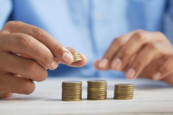 Two hands are making three stacks of golden colored coins