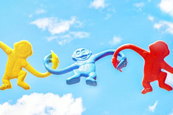 Yellow, blue and red plastic monkey toys have their arms linked together in front of a blue sky, symbolizing fun