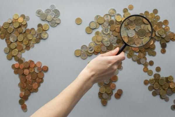 World map made of coins with a person’s hand holding a magnifying glass looking over the general region of Asia