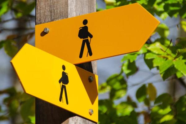 An orange arrow sign and a yellow arrow sign, both with black images of backpackers, pointing in two different directions, implying uncertainty, geopolitical or otherwise
