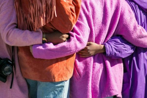 Four people in purple jackets holding hands behind each others backs, showing inclusion